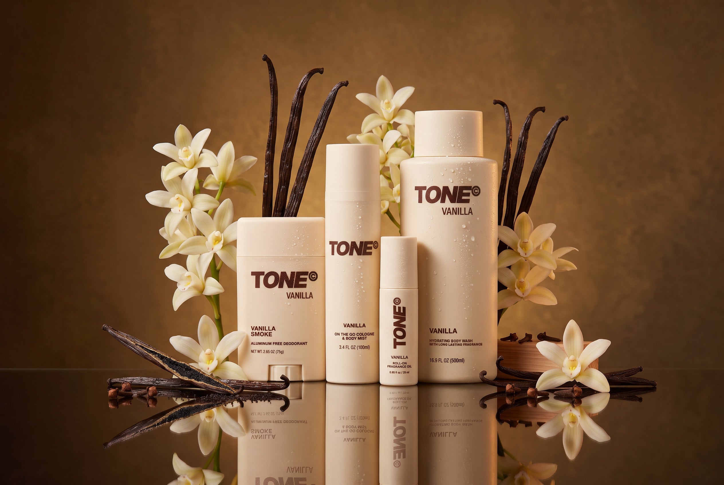 TONE VANILLA body care collection arranged on a reflective dark surface with vanilla beans and vanilla flowers against a warm brown background.